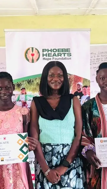 Graduates holding certificates beside their facilitator at the PHHF banner